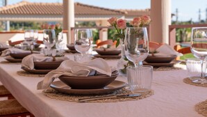 Una mesa preparada para comer, con platos, tazones, vasos y un florero con flores.