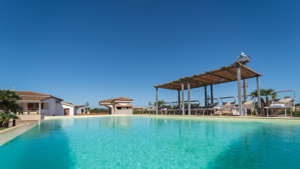 Una piscina azul cristalina con sillas de descanso y un pabellón cubierto.