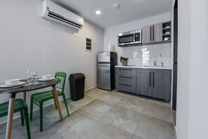 A compact kitchen with a dining area, including a table with chairs, a refrigerator, a microwave, and a trash bin. - Rooftop Pool w/Lounge Area-Studio Sleeps 2 A12 (Oranjestad)