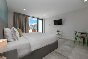 A modern hotel room with a large bed, a TV mounted on the wall, a small table with chairs, and a view of the outside. - Rooftop Pool w/Lounge Area-Studio Sleeps 2 A12 (Oranjestad)
