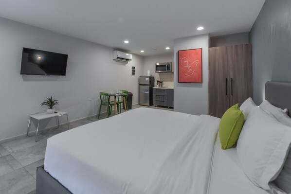 A modern hotel room with a large bed, a small desk, a flat-screen TV, a microwave, and a wardrobe.