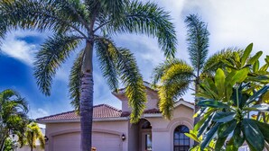 A residential house with a well-maintained lawn, palm trees, and a clear sky.