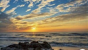 A sunset over the ocean with rocky terrain in the foreground.