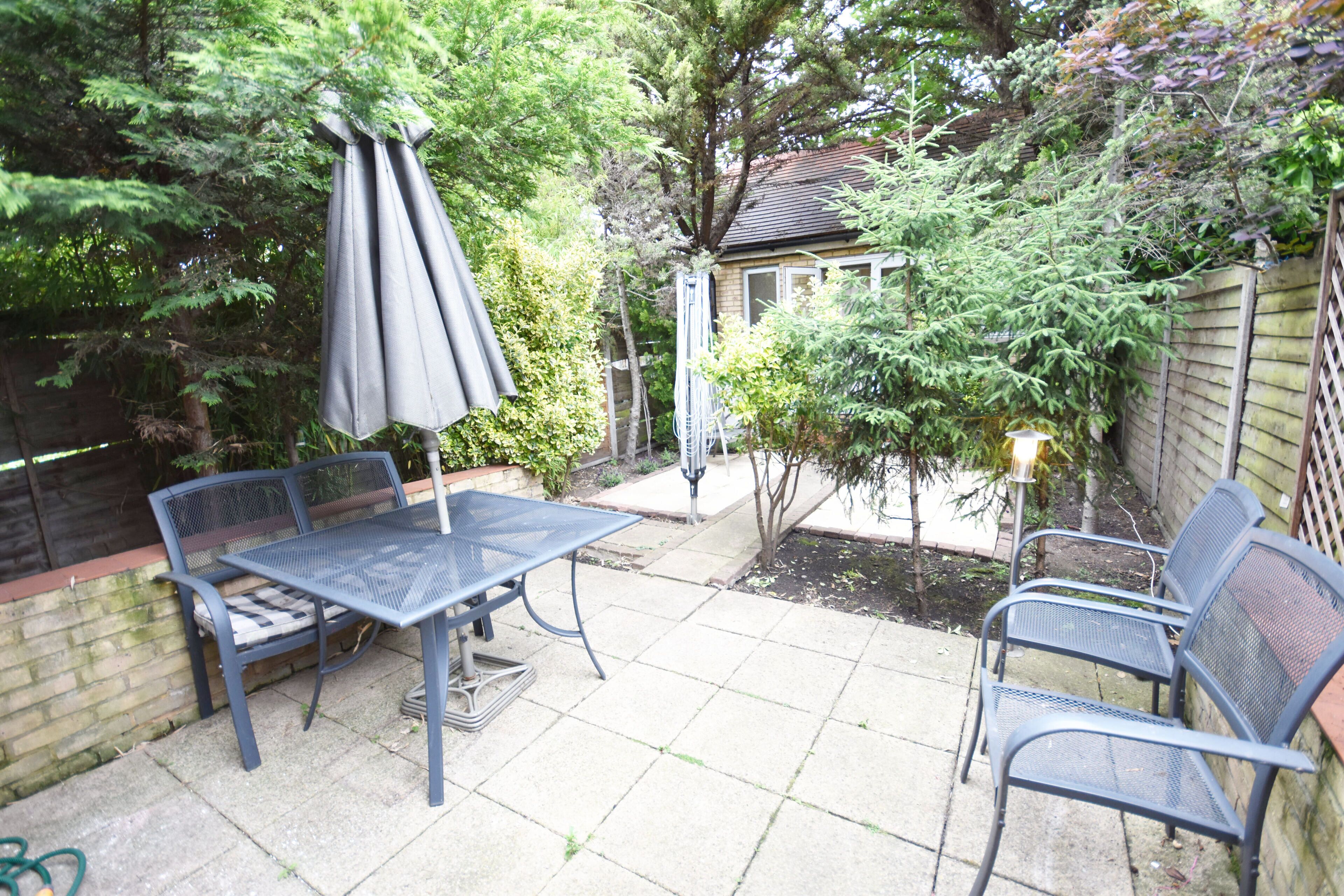 Une terrasse avec une table et des chaises en métal, entourée de verdure et d’une clôture en bois.