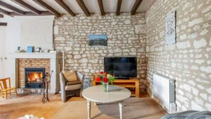 A cozy living room with a stone wall, a fireplace, a television, and a comfortable seating area. - Vacances Gites Assay Maisons Chaleureuse (Assay)
