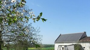 A rural landscape with a white barn, a grassy field, and blooming trees. - Vacances Gites Assay Maisons Chaleureuse (Assay)