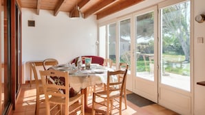 A dining area with a wooden table set for four, surrounded by chairs, with a view of the garden through large sliding glass doors. - Large house for 7 400m from the beach (Sainte-Marie-de-Ré)