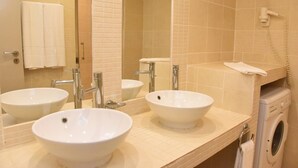 Une salle de bain avec trois lavabos, un miroir, un porte-serviettes et un lave-linge.