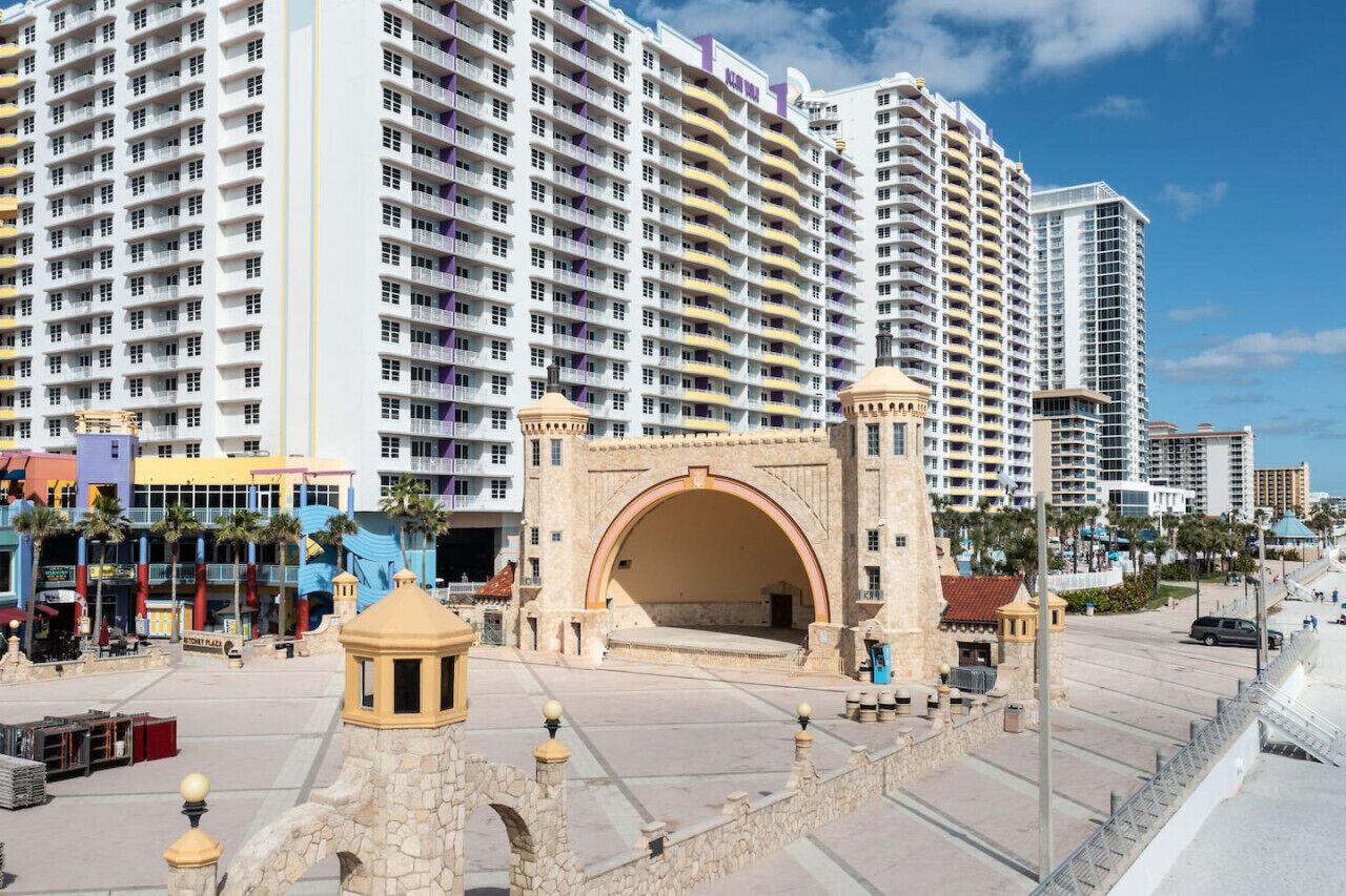 A large hotel with multiple floors and balconies, a prominent archway entrance, and a beachfront location.