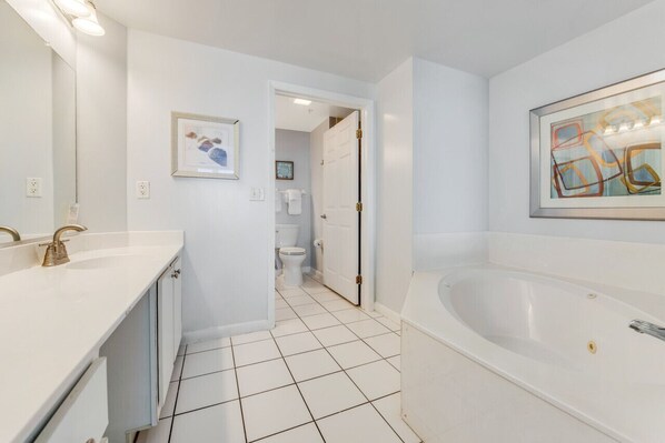 A modern bathroom with a white sink, a bathtub, and a toilet. There is a framed picture on the wall and a door leading to another room.