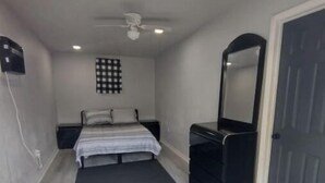 A bedroom with a bed, a dresser, a mirror, a ceiling fan, and a wall-mounted heater. - Backyard Guest House Suite (Gainesville)