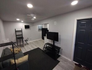 A compact living space with a sofa, a small table, a TV, and a ceiling fan. - Backyard Guest House Suite (Gainesville)
