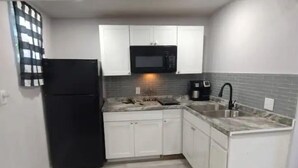A compact kitchen with white cabinets, a black refrigerator, a microwave, a coffee maker, and a sink. - Backyard Guest House Suite (Gainesville)
