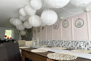 A dining area with a wooden table, white paper lanterns, and floral-patterned wall panels.