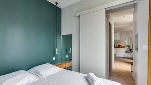 Une chambre d’hôtel moderne avec un grand lit, une table de chevet en bois, un mur d’accent de couleur turquoise et une vue sur la cuisine.