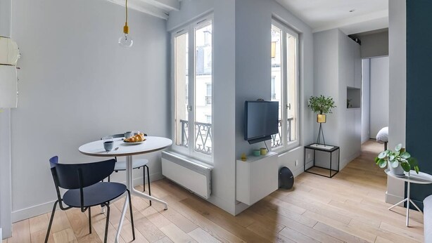 Un salon moderne avec une table ronde, deux chaises, un téléviseur et une fenêtre donnant sur un beau paysage.