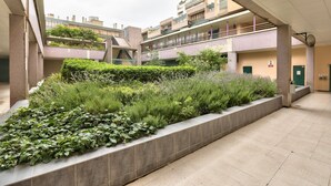 A courtyard with a landscaped garden, a covered walkway, and a building with multiple floors and balconies. - GuestReady - Magnificent Parisian Apartment (Paris)