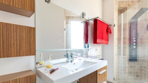 A modern bathroom with a wooden panel wall, a white sink with a glass enclosure, a glass shower enclosure, and a red towel hanging on a towel rack.