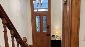 Eine Holztreppe führt zu einem Raum mit einem Chandelier, einer Holztür mit Glasfeldern und einem kleinen Tisch mit einer Lampe.