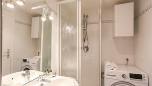 Een moderne badkamer met een grote spiegel, een wastafel, een wasmachine en een douche.