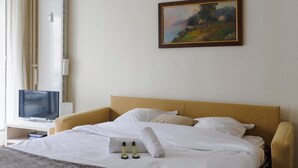 Een hotelkamer met een bed, een schilderij aan de muur, een televisie en een raam met gordijnen.