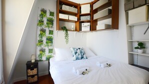 Una camera da letto con un letto, un comodino, uno scaffale con contenitori e una pianta sospesa al muro.