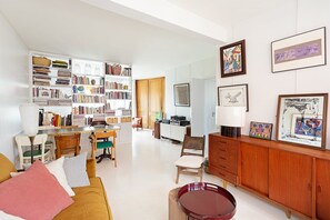 Una sala de estar bien iluminada con un sofá, sillas, una mesa de comedor y una estantería llena de libros.