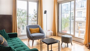 A modern living room with a sofa, armchair, ottoman, and a floor lamp. - GuestReady - Superb Stay in the Heart of Paris (Paris)