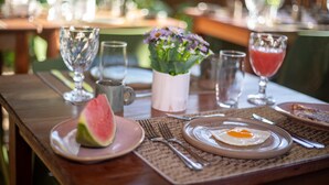 A breakfast table with plates, cutlery, a glass of juice, a glass of water, a glass of wine, and a vase with flowers. - Bella Rosa Noronha (Fernando de Noronha)