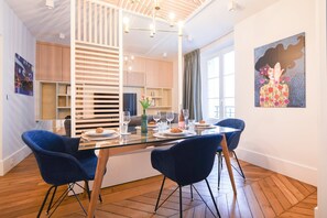 A modern dining area with a glass table, blue chairs, and a decorative painting on the wall. - GuestReady - luxury apt near the Eiffel Tower (Paris)