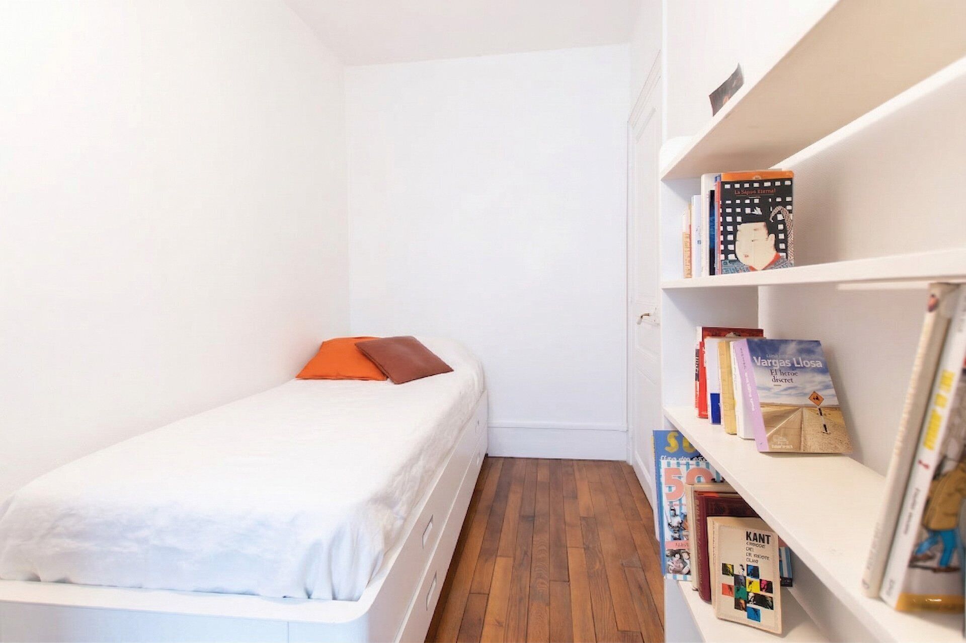 Un dormitorio pequeño con cama, estantería y suelo de madera.