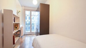 A bedroom with a bed, a bookshelf, a window, and a door leading to a balcony. - GuestReady - Bright Apt in the new Quartier Latin (Paris)
