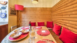 Ein gemütliches Holzhaus-Interieur mit einem Esstisch, der für vier Personen gedeckt ist, roten Kissen und einer roten Lampe.