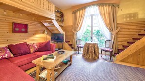 Ein gemütliches Blockhauszimmer mit einer Couch, einem Couchtisch, einem Fernseher und einem Esstisch mit Stühlen.