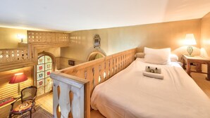 Ein Hotelzimmer mit einem Holzbett, einem Nachttisch mit Lampe, einem Sessel und einem kleinen Tisch ebenfalls mit Lampe.