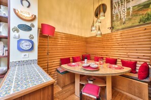 Interior acolhedor de uma cabana de madeira com uma mesa redonda de madeira, almofadas vermelhas e uma pintura de uma floresta.