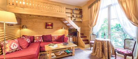 Interior acogedor de una cabaña de madera con un sofá rojo, una mesa de centro de madera, un televisor y una escalera que lleva a un balcón.