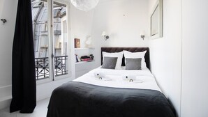 Ein Schlafzimmer mit einem großen Bett, einer Kristallleuchter, einem Fenster mit Blick auf Gebäude und einem Balkon mit Geländer.
