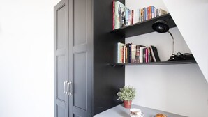 Ein Arbeitsbereich mit Schreibtisch, Bücherregalen, einer Zimmerpflanze, einer Kaffeetasse und einem Teller Essen.