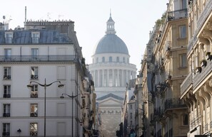 A street view with a prominent white building with a dome in the background, flanked by buildings with balconies and windows. - GuestReady - Cozy and Bright with Notre Dame View (Paris)
