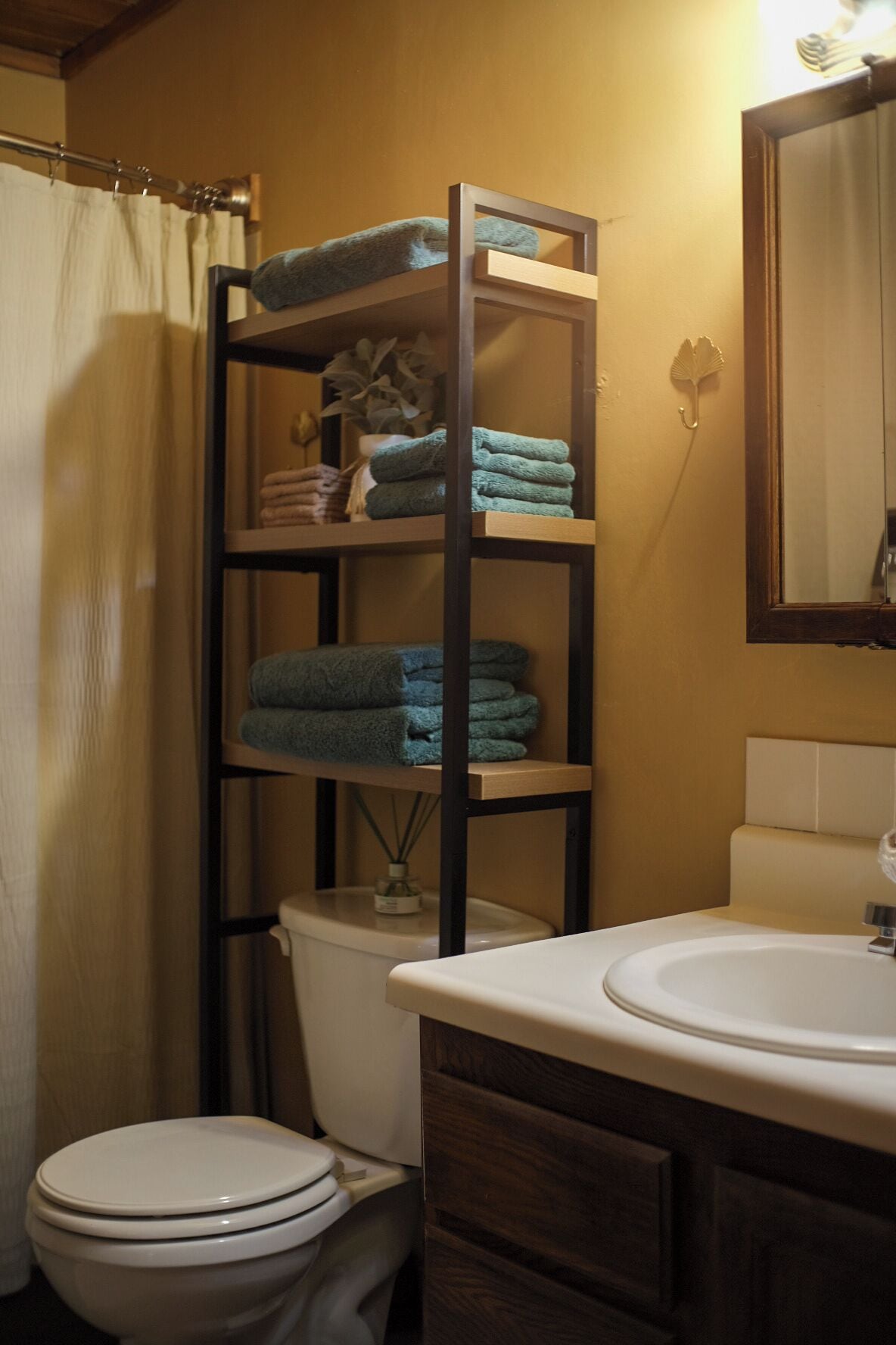 A bathroom with a toilet, a sink, and a shelf with folded towels.