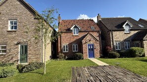 A row of brick houses with a central blue door, a wooden pathway, and a clear sky. - Stunning Coastal Cottage - Sleeping 5 in 2 Bedrooms - Pool and Beach Access Included. (Filey)