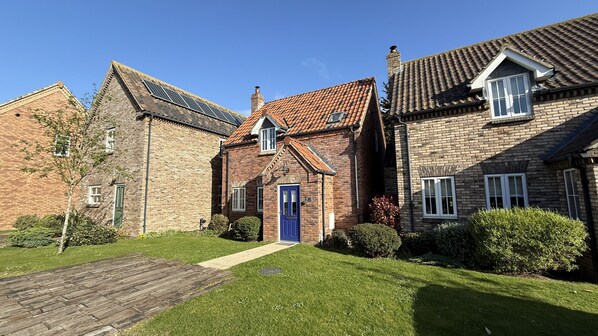 A row of brick houses with a central house featuring a blue door, a tiled roof, and a small garden. - Stunning Coastal Cottage - Sleeping 5 in 2 Bedrooms - Pool and Beach Access Included. (Filey)
