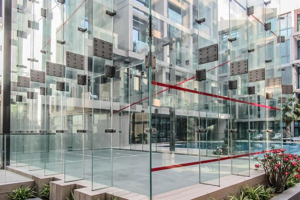 Un edificio moderno con fachada de vidrio, una barrera de cuerda roja y un área de piscina visible a través del vidrio.