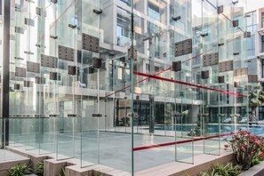 A modern building with a glass facade, a red rope barrier, and a pool area visible through the glass. - Luxurious 1BR Suite Signature Livings in Dubai (Dubai)