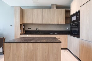 A modern kitchen with wooden cabinets, a granite countertop, and built-in appliances including a microwave and oven. - Luxurious 1BR Suite Signature Livings in Dubai (Dubai)