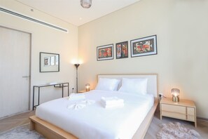 A modern bedroom with a large bed, bedside lamps, a bedside table, and artwork on the wall. - Luxurious 1BR Suite Signature Livings in Dubai (Dubai)