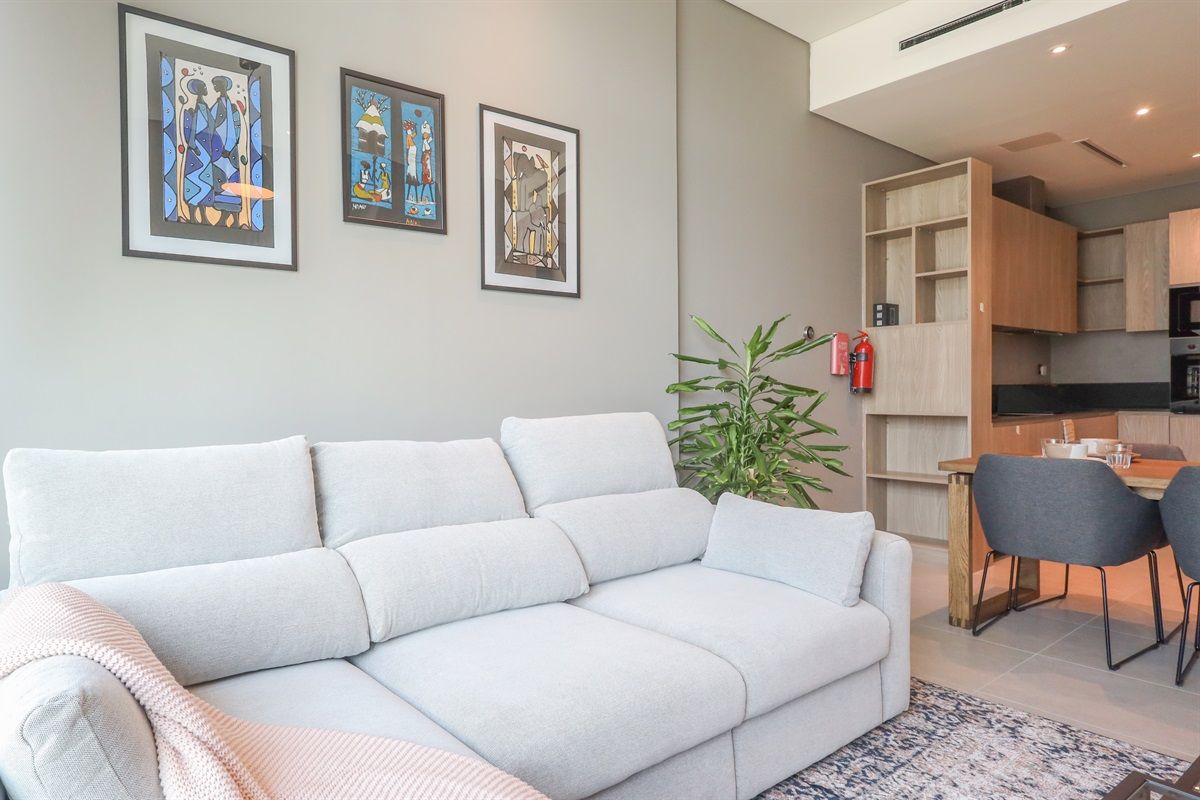 A modern living room with a sofa, a dining area with chairs, and a kitchen with cabinets.