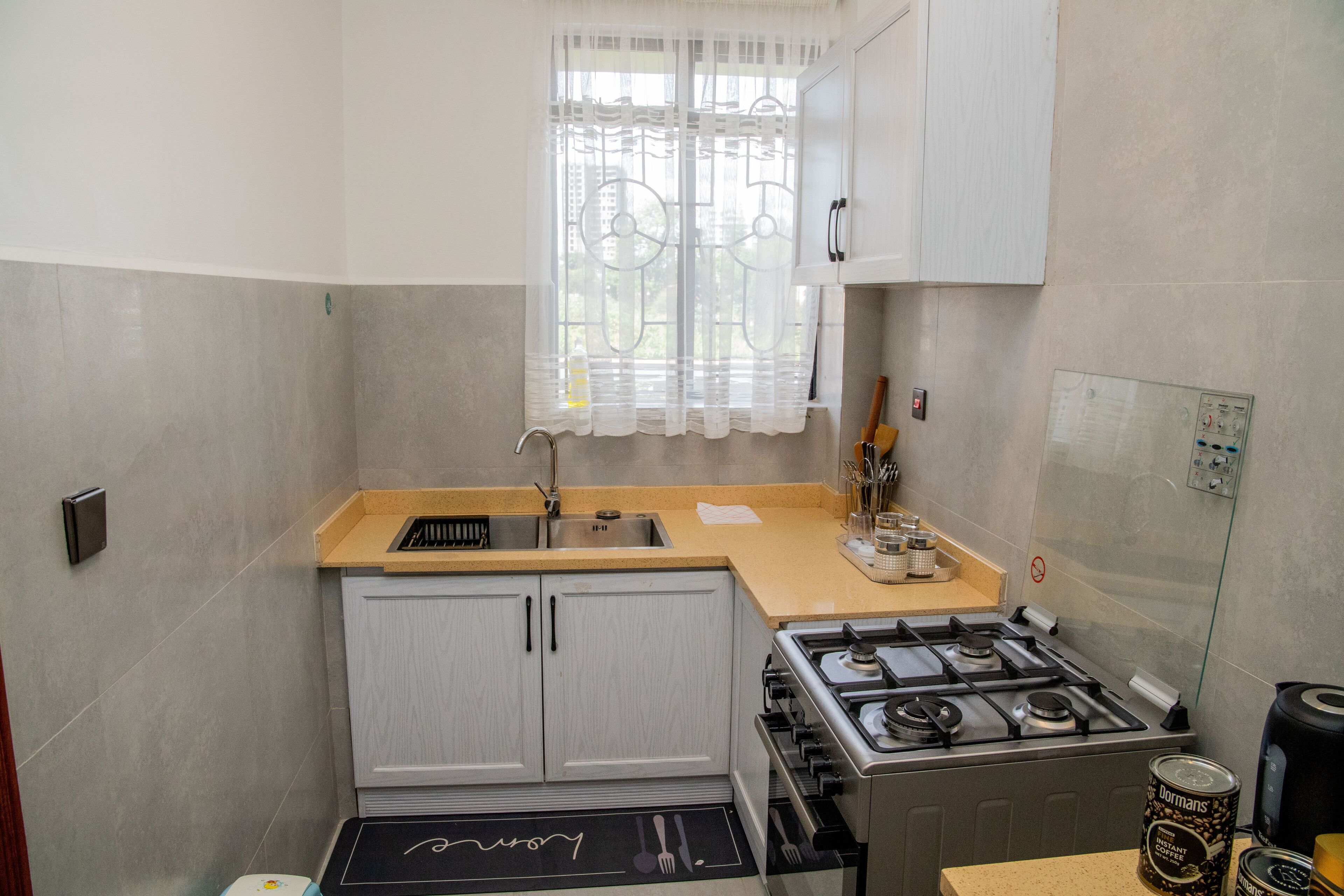 A compact kitchen with a gas stove, a sink, and a window with a decorative curtain.