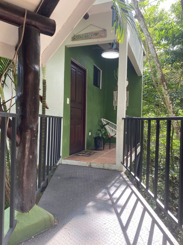 Uma entrada com paredes verdes, porta de madeira, corrimão de metal e planta em vaso.